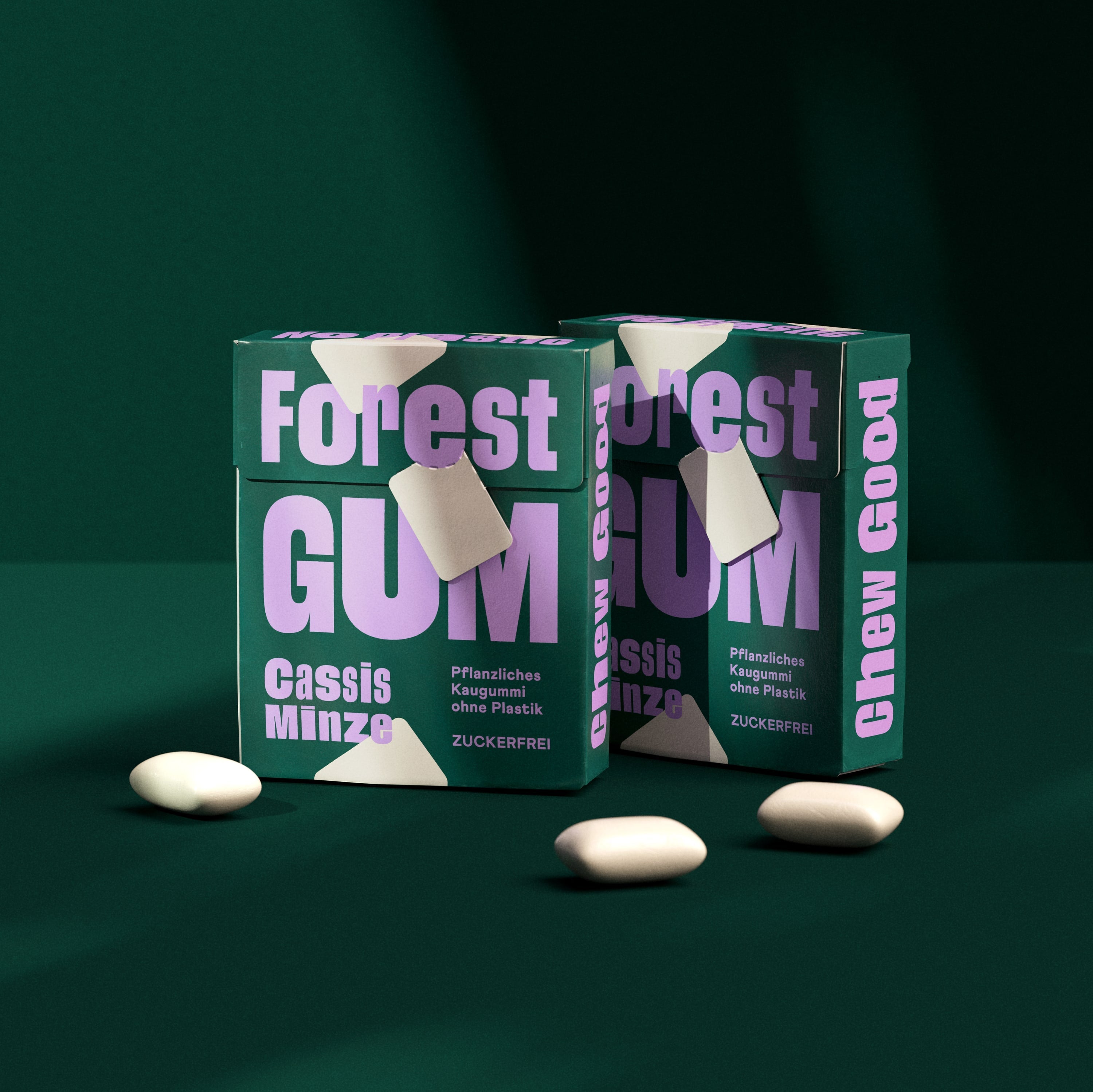 Forest Gum Cassis Minze 2× Kaugummi-Packungen vor grünem Hintergrund, umgeben von Kaugummis.