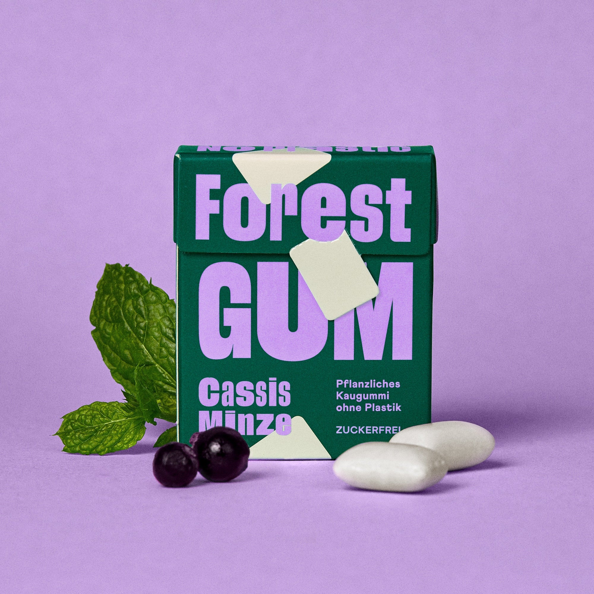 Forest Gum Cassis Minze Kaugummi-Packung, umgeben von Kaugummis, Johannisbeeren und Minzblätter.