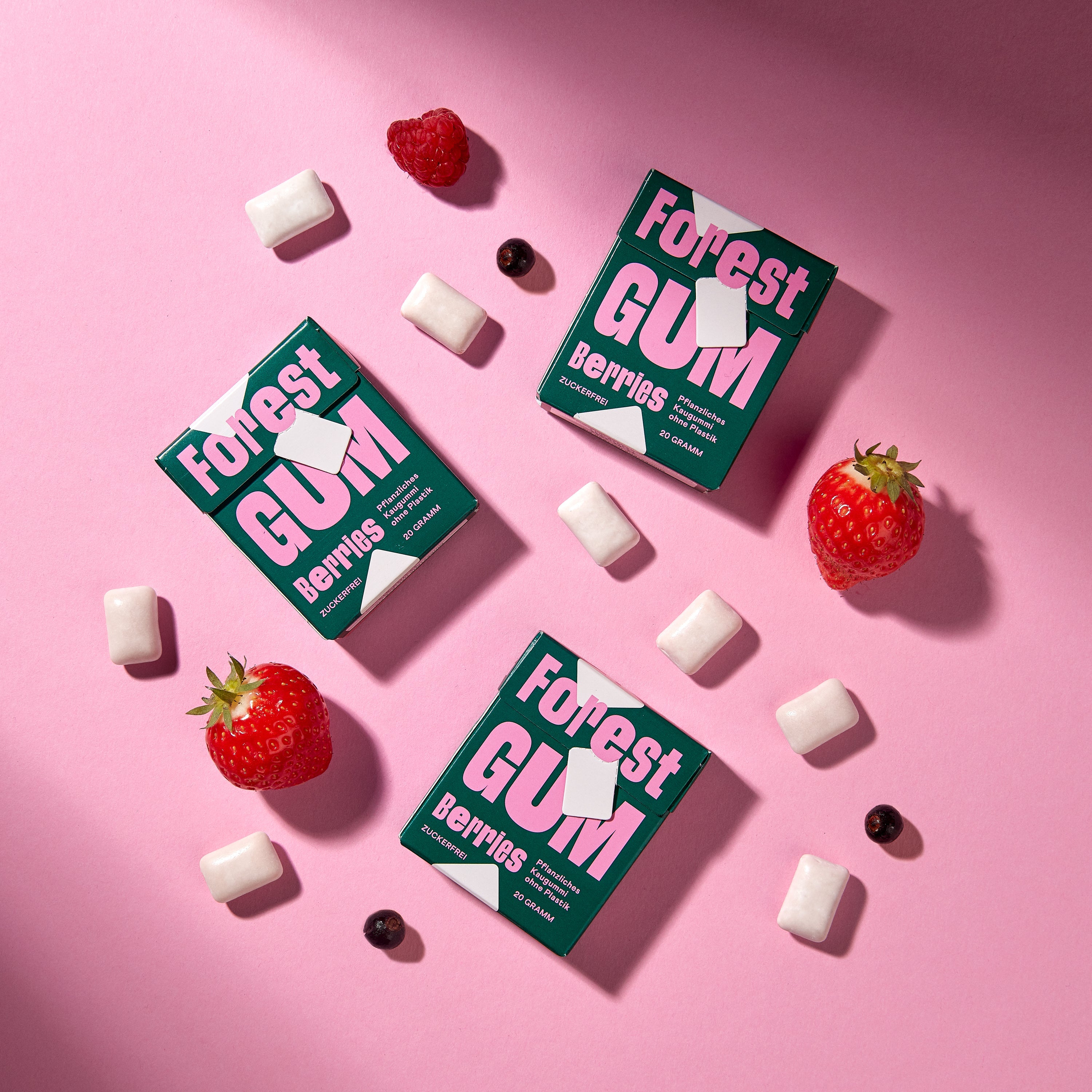 Forest Gum Berries 3× Kaugummi-Packungen, umgeben von Kaugummis, Erdbeeren, Himbeeren & Johannisbeeren.