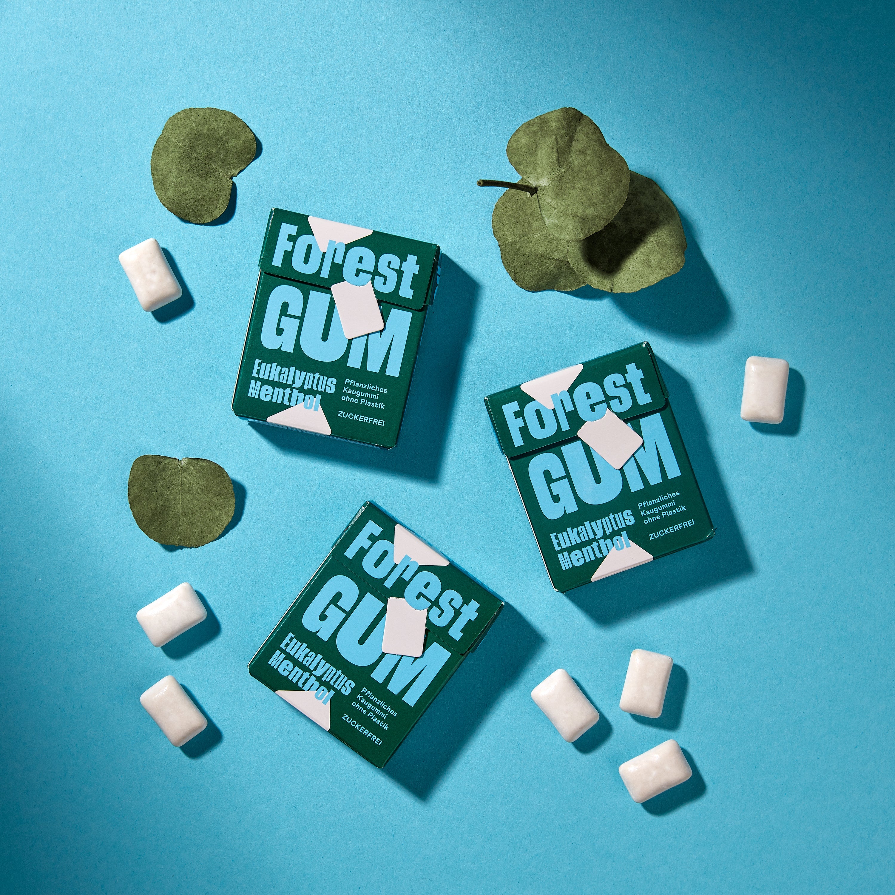 Forest Gum eukalyptus menthol 3× Kaugummi-Packungen, umgeben von eukalyptus blätter.