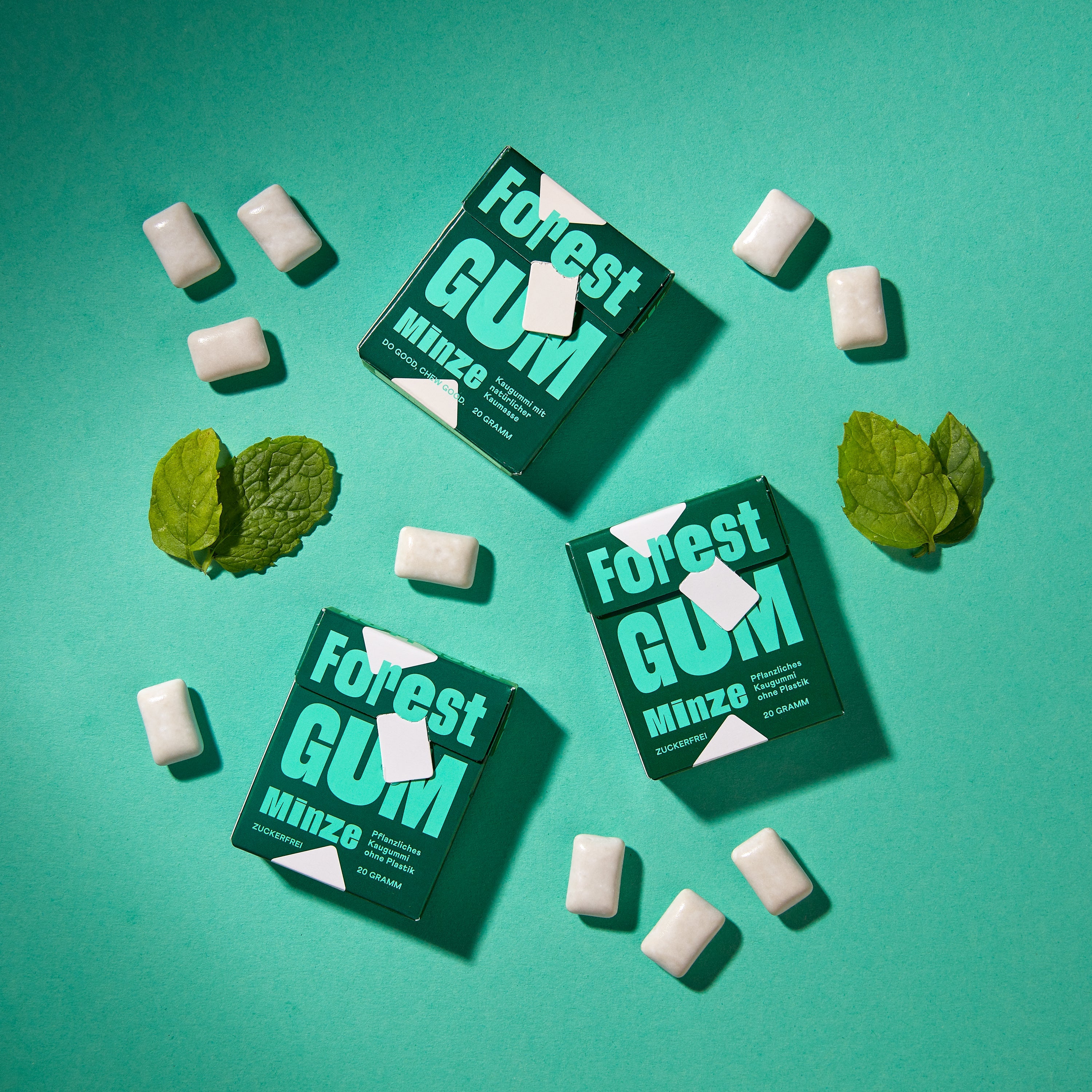 Forest Gum Minze 3× Kaugummi-Packungen, umgeben von Kaugummis und Minz blätter.